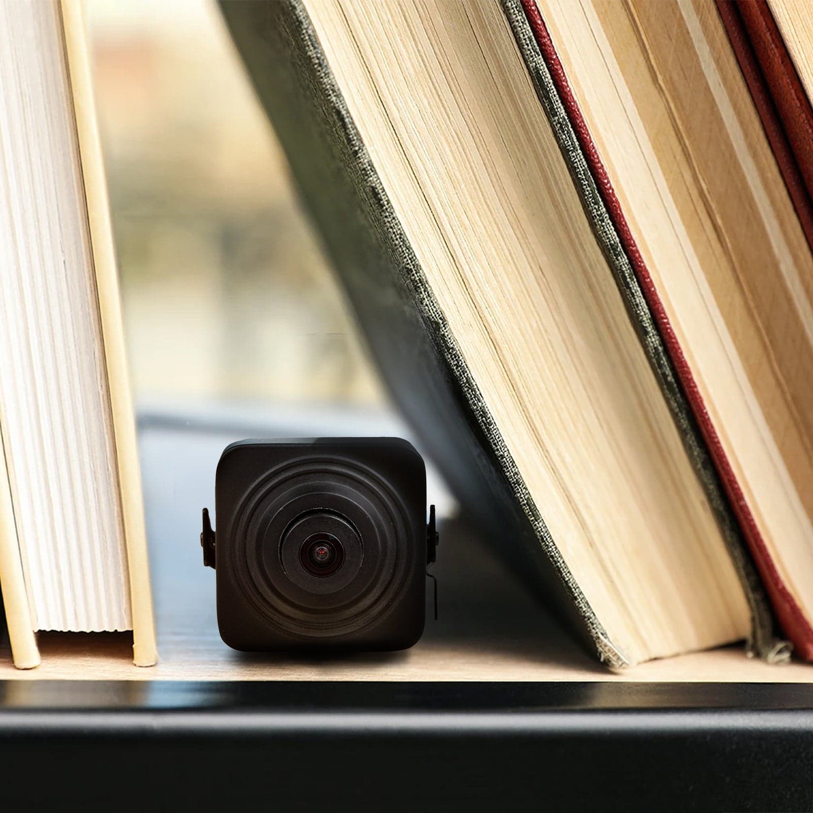 Bolide BN600AI pinhole camera shown in situ on a shelf beside books, illustrating how small the body is - manufacturer lifestyle image